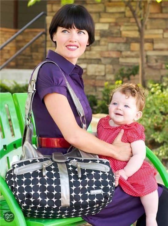 Vrouw met baby en tas op groene bank.