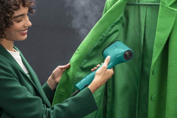 Vrouw stoomt groene jas met handheld stomer.