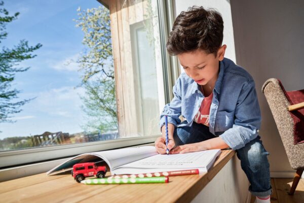 Kind schrijft in boek bij raam met speelgoedauto.