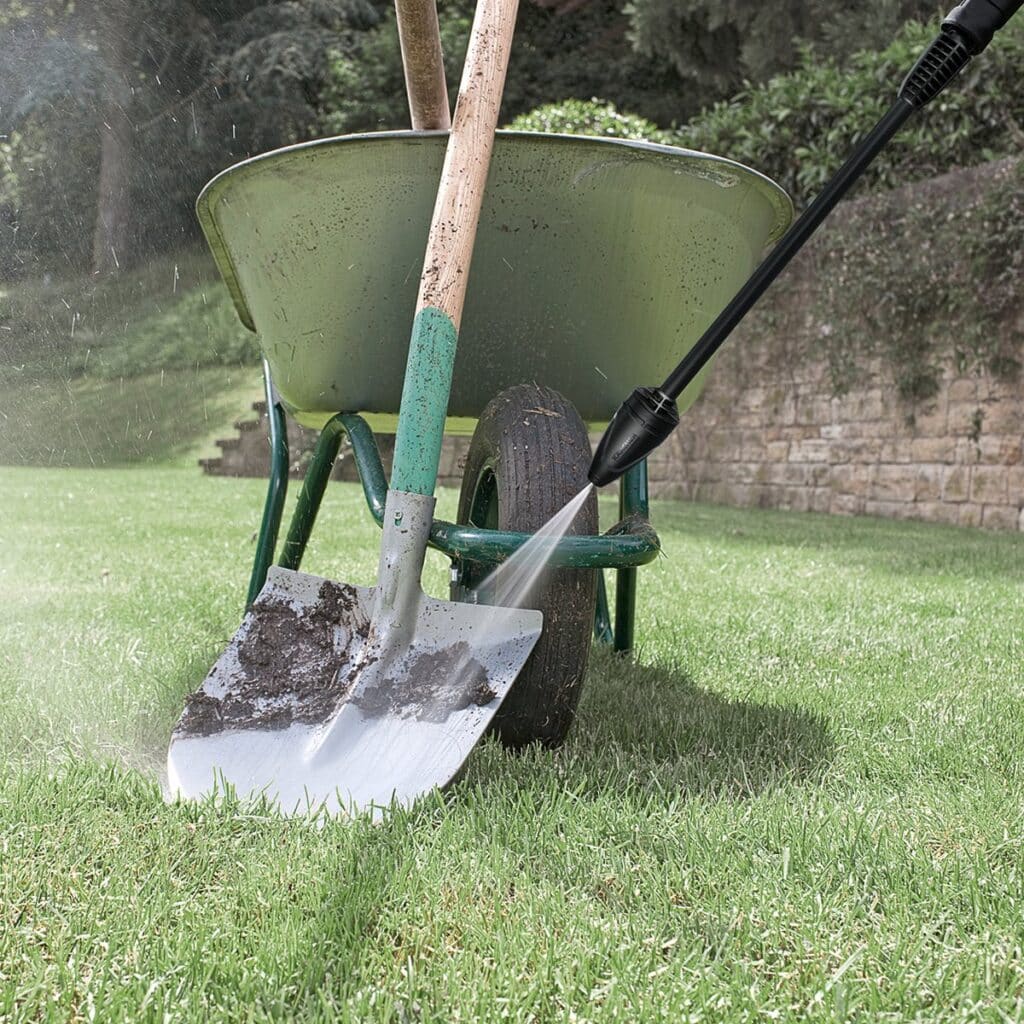 Hogedrukreiniger reinigt vuile spade en kruiwagen op gras.