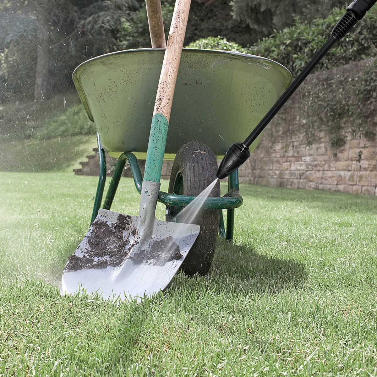Hogedrukreiniger reinigt vuile spade en kruiwagen op gras.