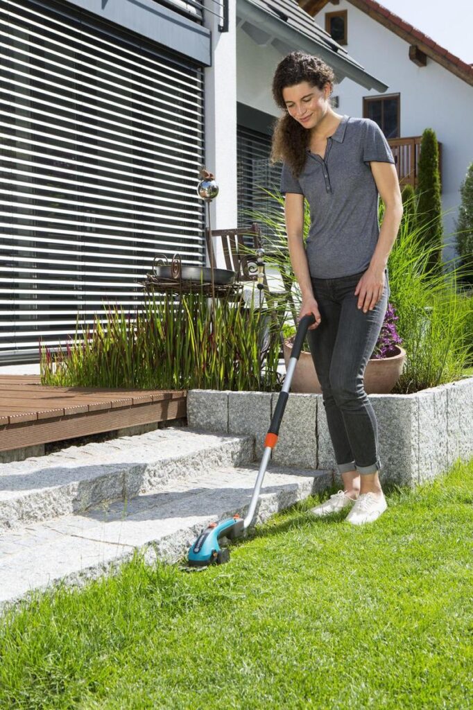 Persoon trimt gras bij terras met grastrimmer.