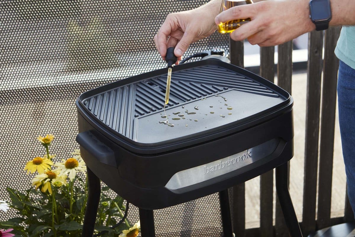 Man voegt olie toe aan barbecue grillplaat.