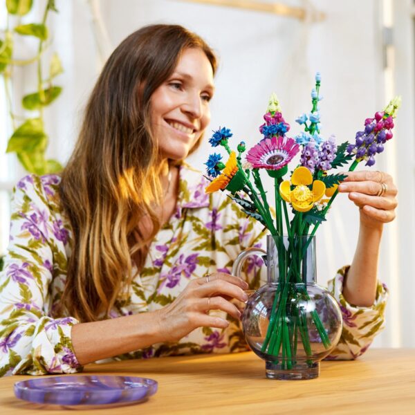 Vrouw rangschikt kleurrijke bloemen in glazen vaas.