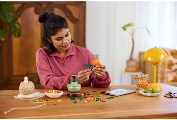 Vrouw bouwt LEGO bloem aan tafel.