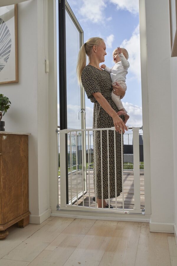 Vrouw met baby bij veiligheidshekje thuis.