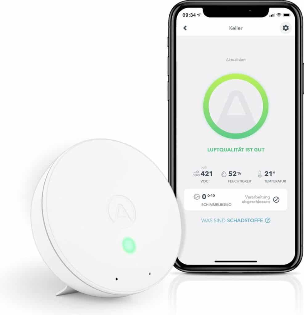 Luchtkwaliteitsmonitor naast smartphone met app geopend.