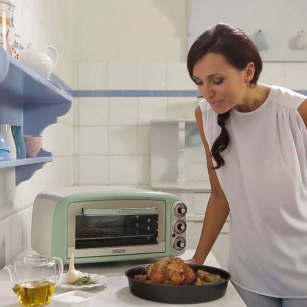 Vrouw bekijkt gebraden kip bij mini-oven in keuken.