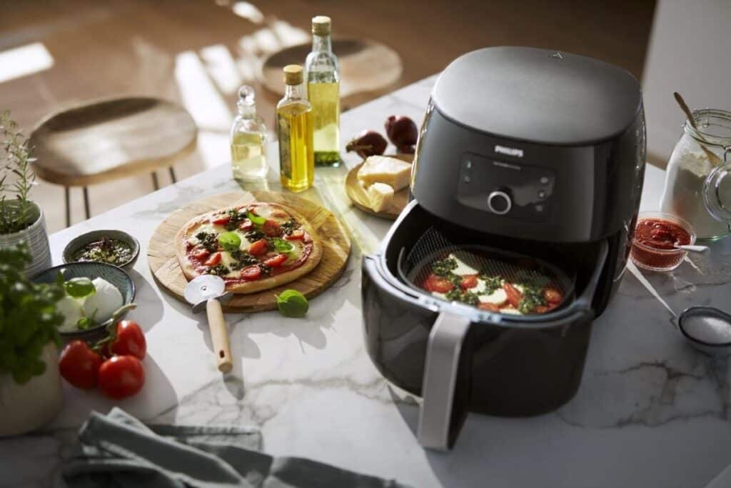 Airfryer met pizza op keukenblad vol ingrediënten.
