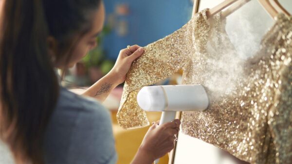 Vrouw stoomt gouden glitterjurk met kledingstomer