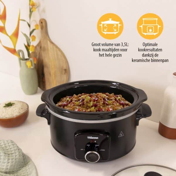 Zwarte slowcooker met een stoofgerecht op keukentafel.