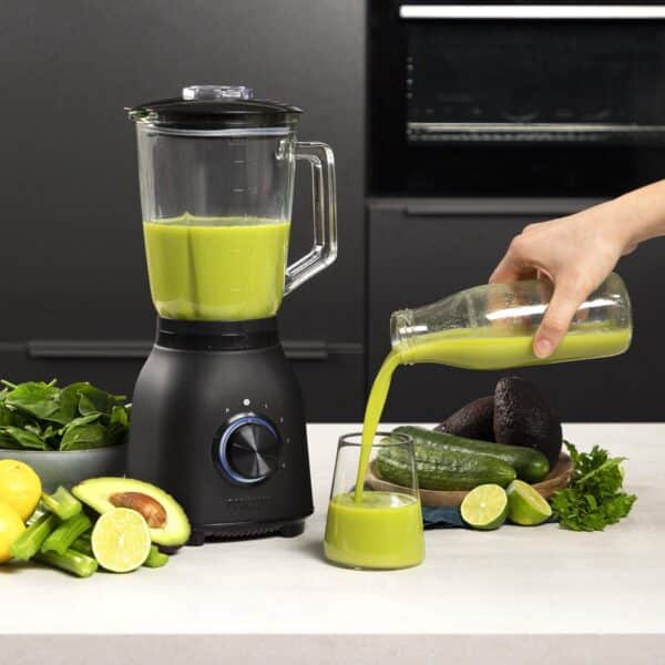 Groene smoothie wordt geschonken in een glas bij blender.