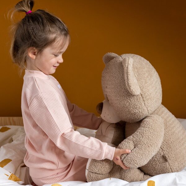 Kind knuffelt grote teddybeer op bed.