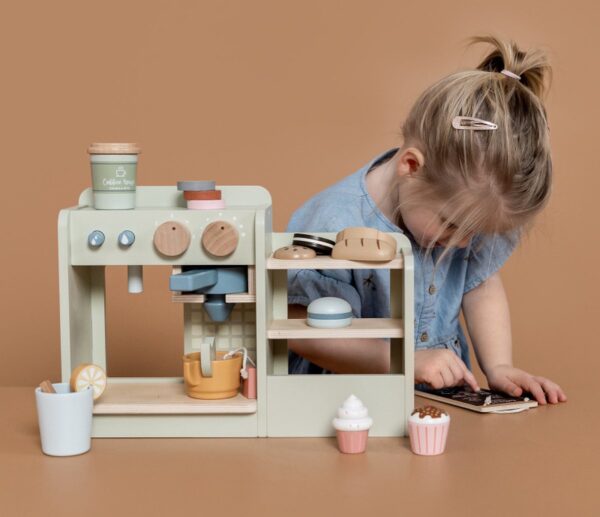 Kind speelt met speelgoedkoffiezetapparaat en bakkerijitems.