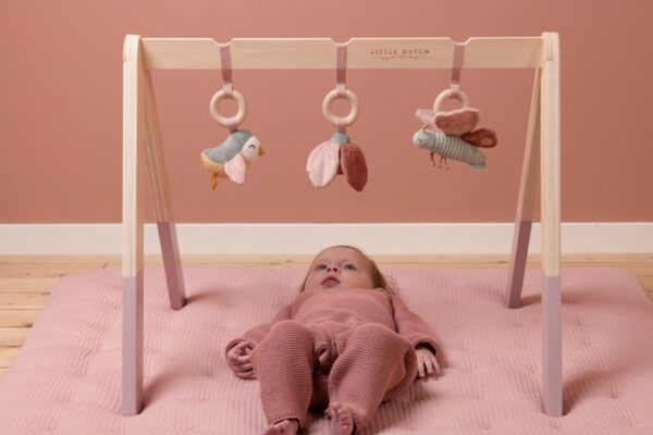 Baby speelt onder houten speelboog met hangspeeltjes.