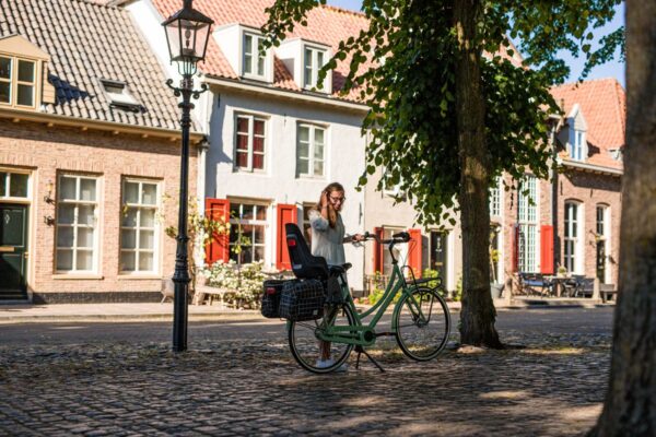 Vrouw met fiets in zonnige straat met huizen.