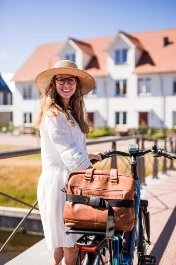 Vrouw met hoed en fiets op brug in zonlicht.