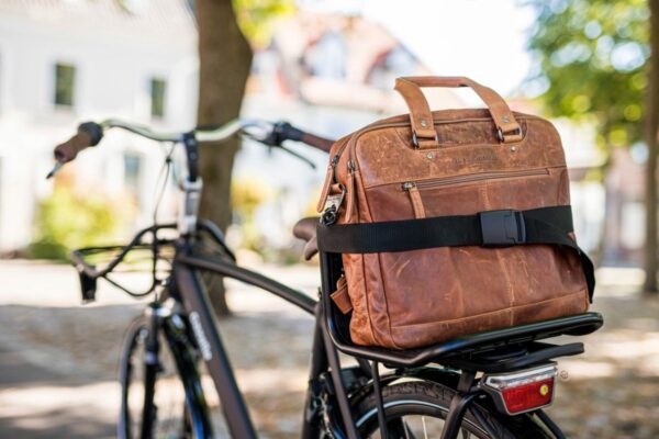 Leren tas op fietsdrager in zonnige straat.