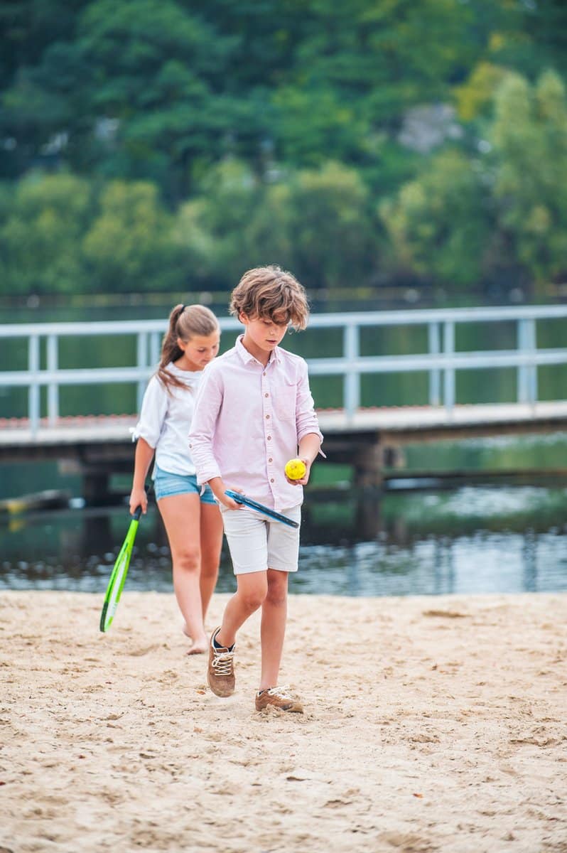 Kinderen spelen op zandstrand met rackets en ballen.