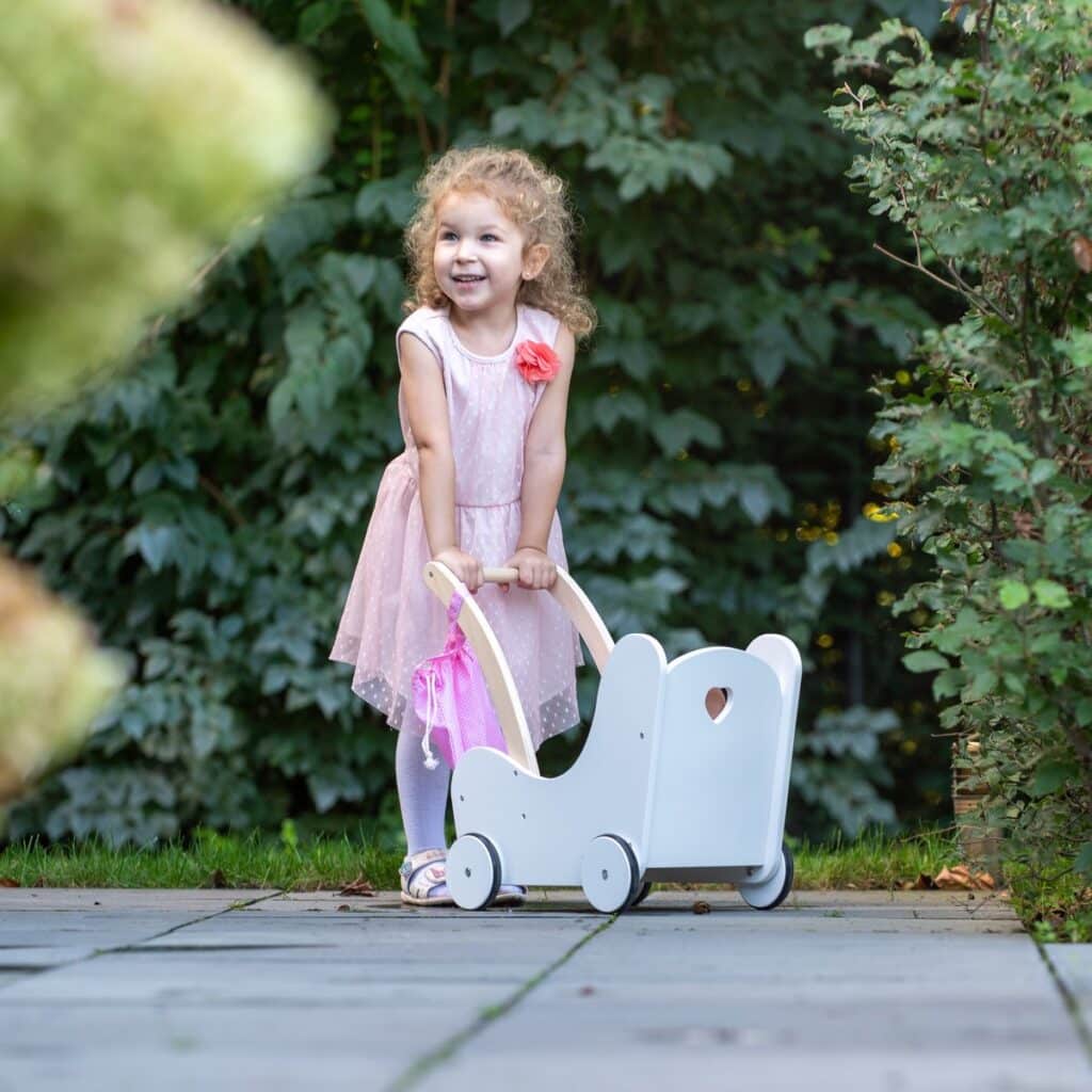 Kind met houten poppenwagen in tuin.