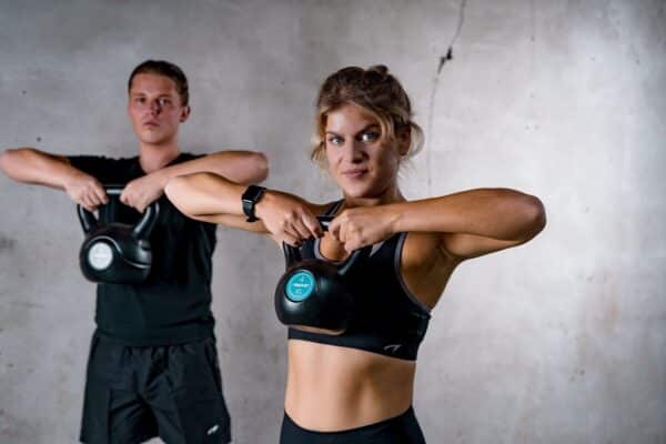 Twee mensen trainen met kettlebells binnen.