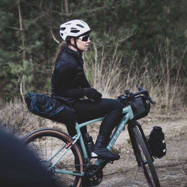 Vrouw mountainbiken op landweg met helm en bril.