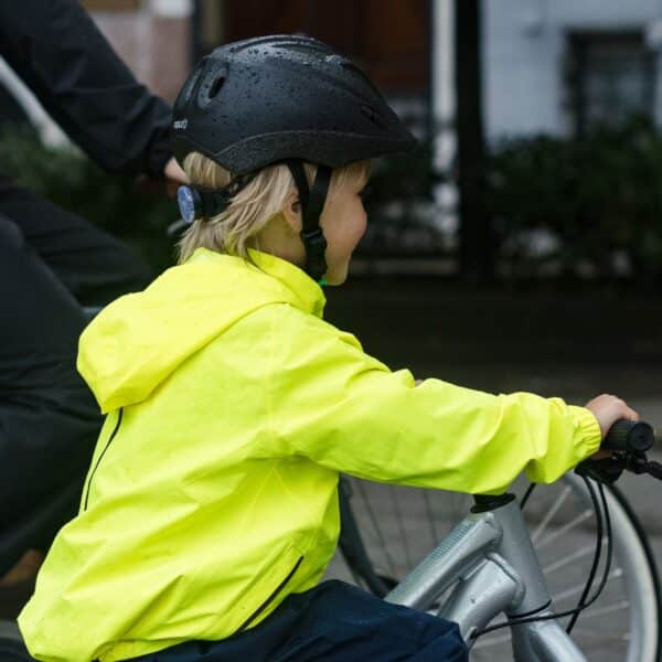 Kind op fiets met regenjas en helm.