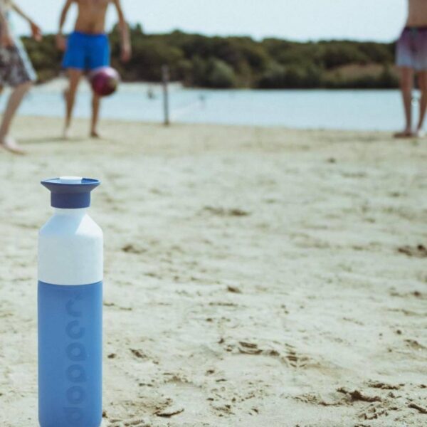 Blauwe waterfles op strand met mensen op achtergrond.