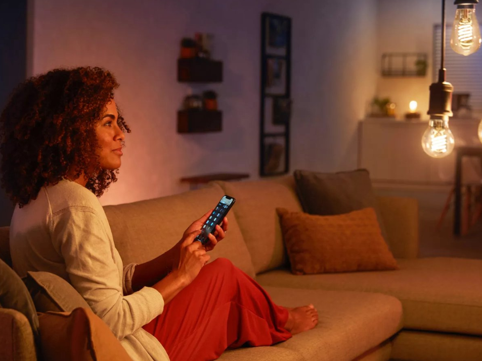 Vrouw bedient verlichting met smartphone in gezellige woonkamer.