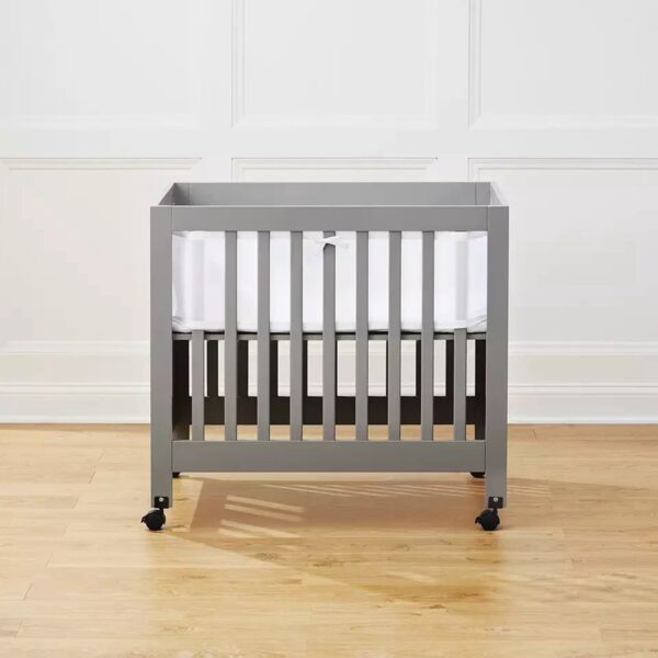 Grijs babybed met wielen in lege kamer.