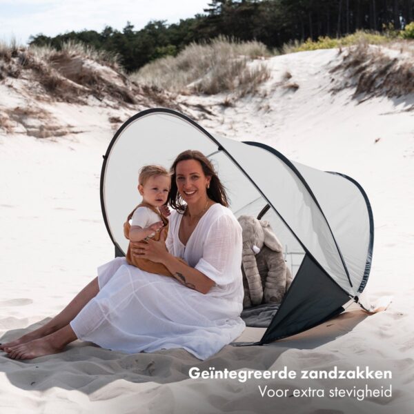 Moeder en kind in tent op zandduinstrand.