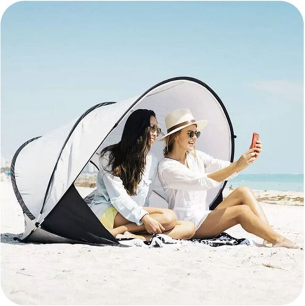 Twee vrouwen maken selfie op strand in schuiltent.