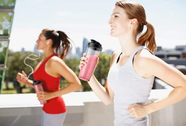 Twee vrouwen joggen en drinken smoothie buiten.