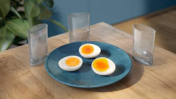 Gekookte eieren op blauwe schaal met drie glazen water.