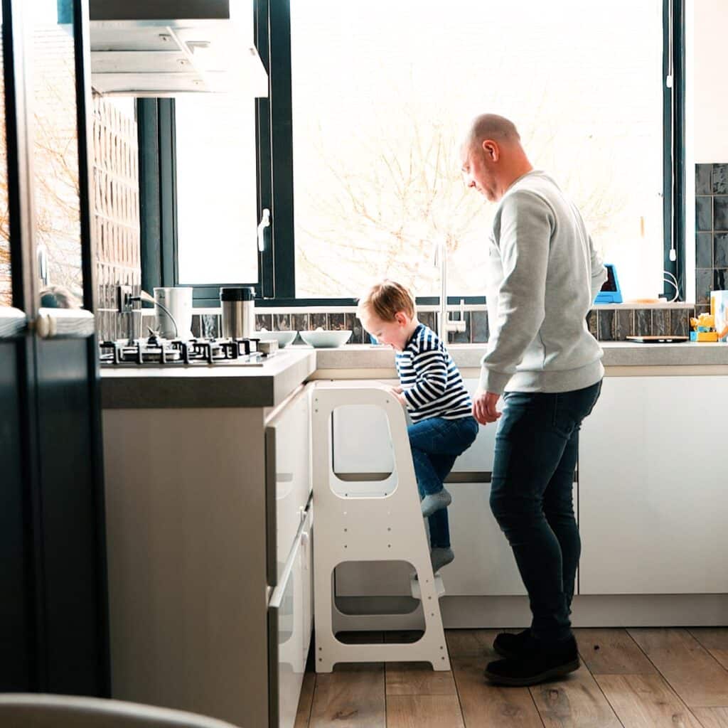 Vader helpt kind in keuken op trapkruk.